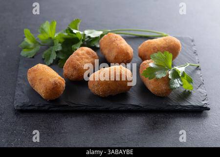 Gebratene Kabeljaukroketten auf schwarzem Schiefergrund Stockfoto