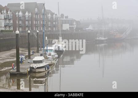 Anlegeboote und Yachten am Ufer des Flusses Arun in Littlehampton, West Sussex, England. Ebbe, todruhig und sehr nebelig. Stockfoto