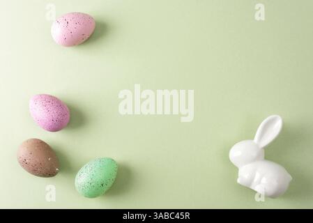 Gesprenkelte Ostereier und weißer Häschen auf grünem Hintergrund. Draufsicht, flach, Kopierbereich. Stockfoto