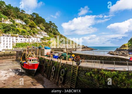 Das Fischerboot liegt bei Ebbe im Hafen von Polperro, mit Sichtbarkeit der Meeresmauer und der Küste. Stockfoto
