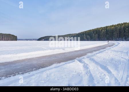 Schlittschuhlaufen auf einem gefrorenen Teich in Sysert, Russland, umgeben von einer verschneiten Landschaft und Kiefernwald. Eine Person genießt Winteratmosphäre in der Stadt Stockfoto