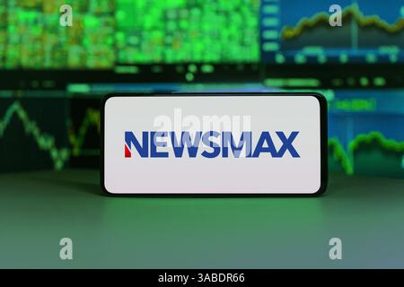 Newsmax Nahaufnahme des Smartphone-Bildschirms mit dem Newsmax-Logo und Börsendiagrammen im Hintergrund, die Medien, Finanzen und Nachrichten darstellen Stockfoto