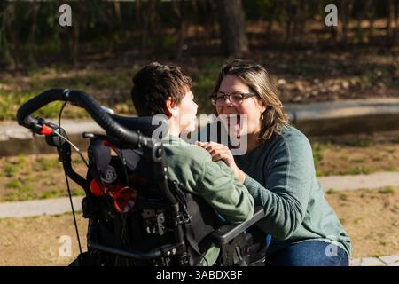 Mutter hat Spaß mit einem behinderten Sohn im Rollstuhl im Park Stockfoto