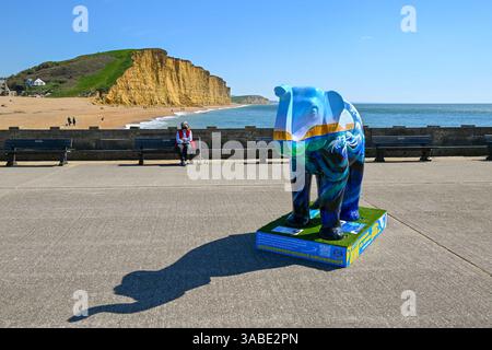 West Bay, Dorset, Großbritannien. April 2025. Wetter in Großbritannien. Eine farbenfroh bemalte Elefantenskulptur, die Teil des Kunstwegs Stampede by the Sea in West Bay in Dorset ist, an einem Tag mit heißem Frühlingssonne und klarem blauem Himmel . Bildnachweis: Graham Hunt/Alamy Live News Stockfoto