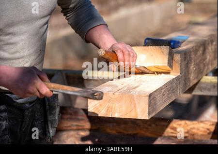 Facharbeiter, der an einem klaren sonnigen Tag Holz mit Werkzeugen im Freien formt. Stockfoto
