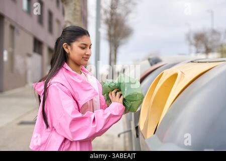 Junge Frau, die Müll in Recyclingbehälter wirft, fördert Umweltbewusstsein Stockfoto