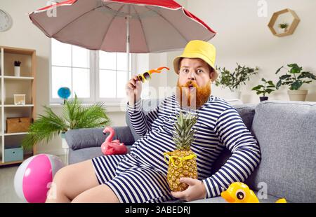 Lustiger Mann, Der Sich Auf Der Couch Mit Einem Cocktail Zu Hause Im Sommer-Outfit Entspannt Stockfoto