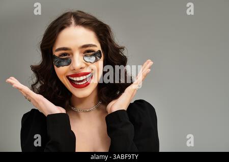 Eine strahlende junge Frau zeigt ihre Zahnspange und ihre hellroten Lippen und strahlt Charme auf grauem Hintergrund aus. Stockfoto