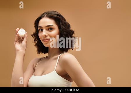 Hübsche junge Frau zeigt ihre Schönheit und Hautpflege Routine, während sie lächelt und ein Produkt hält. Stockfoto