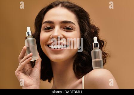 Hübsche junge Frau zeigt ihre Hautpflegeroutine, während sie in einem hellen Studio lächelt. Stockfoto