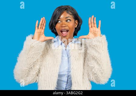 Studio-Porträt einer überraschten jungen Frau, die mit ihren Händen auf blauem Hintergrund Gesten zeigt Stockfoto