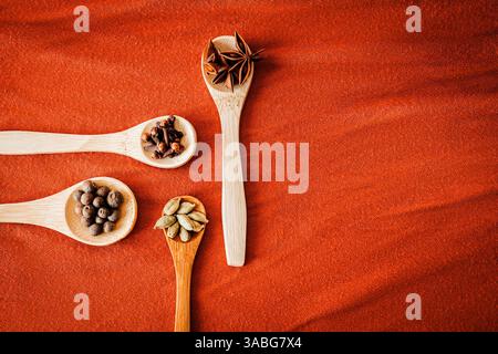 Holzlöffel mit Gewürzen auf warmem orangenem Stoff. Flach liegend mit gemütlichem kulinarischem Flair, perfekt für Herbstkochen, Kräutertees und saisonale Speisen Stockfoto