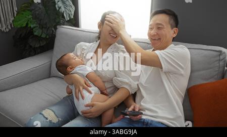 Chinesische Familie genießt spielerische Momente mit Mutter, Vater und Baby auf der Couch im gemütlichen Wohnzimmer des modernen Apartments. Stockfoto