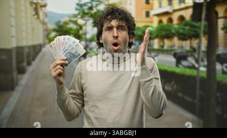 Hispanischer Mann, der polnische Zloty-Banknoten auf einer Stadtstraße mit einem überraschenden Ausdruck hält, der die finanziellen Entdeckungen in einer urbanen Outdoor-Umgebung hervorhebt Stockfoto