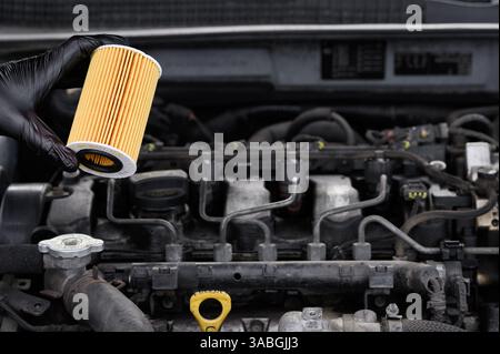 Automechaniker hält Autoölfilter in der Hand auf dem Hintergrund des Motorraums des Autos, Nahaufnahme. Konzept der Durchführung von Wartungsarbeiten Stockfoto