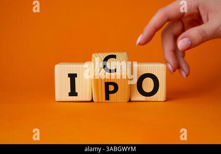 ICO vs. IPO-Symbol. Geschäftsmann zeigt auf gedrehte Holzwürfel mit den Worten IPO und ICO. Wunderschöner orangefarbener Hintergrund. ICO vs IPO und Geschäftskonzept Stockfoto