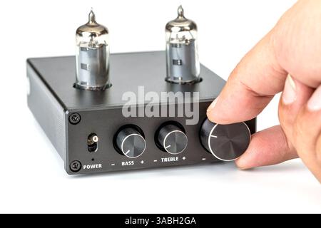 Feinabstimmung eines Röhrenverstärkers: Fokussierte Aufnahme einer Person, die den Lautstärkeregler eines schwarzen Verstärkers anpasst, um Präzision und Kontrolle zu betonen. Stockfoto