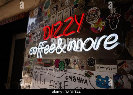 Lviv, Ukraine - 01. April 2025: Farbenfrohe Neonschilder, die für Dizzy Coffee Shop werben, umgeben von kreativen Wanddekorationen Stockfoto