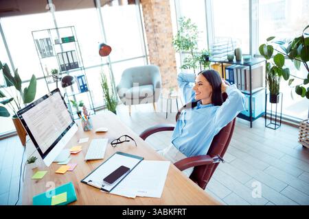 Junge professionelle Frau, die sich in einem modernen Büro entspannt, umgeben von einem produktiven Arbeitsplatz mit natürlichem Licht und lebendigen Pflanzen Stockfoto