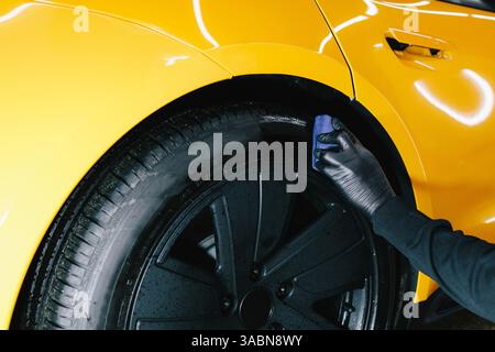Schwärzung des Reifenrads des Autos mit Schwamm mit chemischer Schwärzung des Gummis bei der Detaillierung des Autoservice. Der Mechaniker wendet ein Produkt auf einen schwarzen Reifen an Stockfoto
