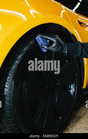 Schwärzung des Reifenrads des Autos mit Schwamm mit chemischer Schwärzung des Gummis bei der Detaillierung des Autoservice. Der Mechaniker wendet ein Produkt auf einen schwarzen Reifen an Stockfoto