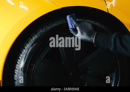 Schwärzung des Reifenrads des Autos mit Schwamm mit chemischer Schwärzung des Gummis bei der Detaillierung des Autoservice. Der Mechaniker wendet ein Produkt auf einen schwarzen Reifen an Stockfoto