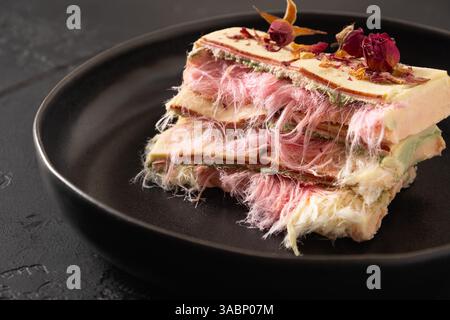 Trendige weiße, rosafarbene Schokolade mit Schicht rosa Pismaniye in Teller auf schwarzem Hintergrund. Leckeres delikates Dessert. Nahaufnahme. Stockfoto