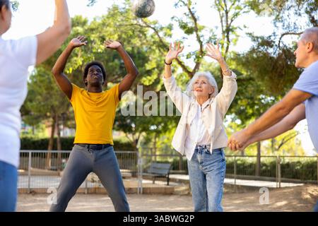 Alte multinationale Menschen spielen Volleyball-Aktivität auf einem Sommerspielplatz für Sport im Frühling draußen Stockfoto