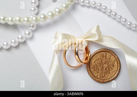 Eheringe gebunden mit Band, Liebesbrief und Perlenkette auf hellem Hintergrund, flache Lay Stockfoto