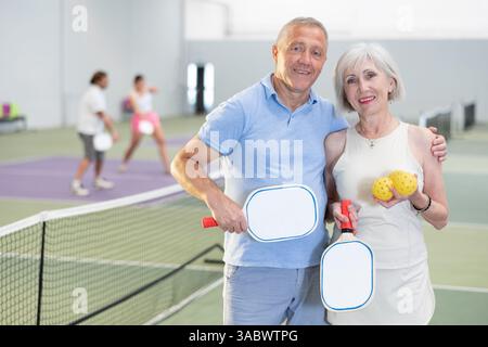 Ältere Ehepaare mit Schlägern und Bällen, die auf dem Pickleball-Platz posieren Stockfoto