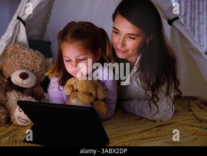 Tablet, Zelt und Mutter mit Kind zu Hause, die Lernspiele oder Online-Aktivitäten zum Binden spielen. Teddybär, Decke Festung und Mutter mit Mädchen Kind Stockfoto
