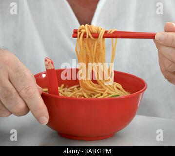 Die Person isst Nudeln mit Stäbchen aus der roten Schüssel. Stockfoto