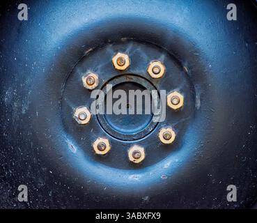 Ein detaillierter Blick auf eine Radnabe mit zahlreichen Bolzen, die die Textur und Handwerkskunst von Metall vor dunklem Hintergrund zeigt. Stockfoto