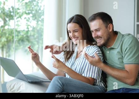 Hoffnungsvolles Paar, das die Finger drückt, um zu Hause die Inhalte des Notebooks zu überprüfen Stockfoto