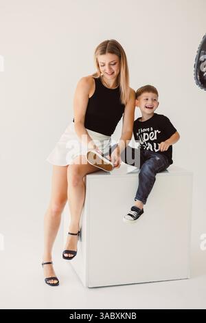 Ein freudiger Moment fängt eine Mutter und einen Sohn in einem hellen Studio ein, die ihre liebevolle Bindung durch ein herzliches Lächeln und Lachen zum Ausdruck bringen und ein herzliches Herz erzeugen Stockfoto