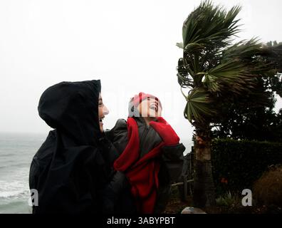 (VERÖFFENTLICHT 01.03.2006, B-8) NSWindyWetWeather250626x003 - Schuss 1/2/06 - Samar Shamieh (CQ), links von Encinitas, umarmt ihren 5-jährigen Sohn Rami Ibrahim, während er über dem Wind schreit, während beide dem starken Wind und Regen vom Parkplatz am Swamis Beach in Encinitas am Montag Morgen gegenüberstehen. Shamieh wollte einen Spaziergang machen, um das Wetter zu genießen und die hohe Brandung zu sehen. Stockfoto