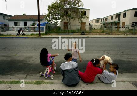 (Veröffentlicht 08.03.2003, A-1; Signon: 08.04.2003): ANA Kiya, 6, links, sitzt auf ihrem Fahrrad, mit Nachbarin Cherry Sovann, 15, und Cousins, Natalya Goban, 4, Patience Goban, 11, und Kye Goban, 6, rechts, während der Nachbar Luis Julian Aguayo, 12, mit dem Fahrrad auf dem Bürgersteig vor seinem Haus in der Gloria Street 424 fährt. Die Kinder, die auf dem Bürgersteig sitzen, leben alle auf der Ostseite der Gloria Street und werden nicht umgesiedelt, aber Luis Aguayo lebt auf der Westseite, die abgerissen wird, um Platz für eine wiederaufgebaute Lincoln High School zu schaffen. Die Wohnungsbewohner nebenan bei 406-420 Glor Stockfoto