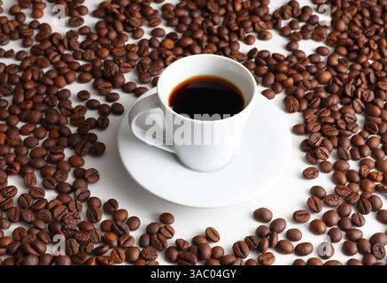Dampfender schwarzer Espresso in einer weißen Tasse, umgeben von gerösteten Bohnen, bringt Wärme, Aroma und den Komfort von morgendlichen Ritualen Stockfoto