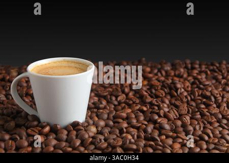 Aromatische Kaffeebohnen umgeben eine weiße Tasse mit heißem Espresso auf dunklem Hintergrund Stockfoto