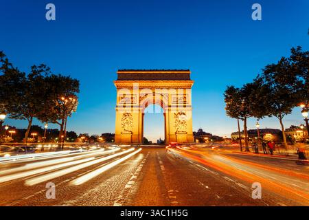 Der beleuchtete Arc de Triomphe in Paris, eingerahmt von lebhaften Lichtpfaden und vor einem tiefblauen Himmel in der Dämmerung Stockfoto