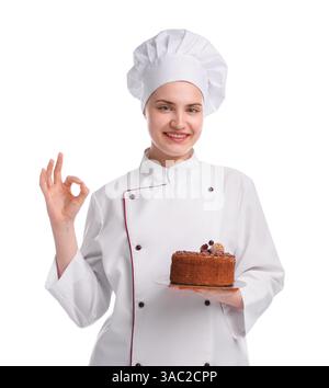 Glücklicher Konditor in Uniform, der leckeren Schokoladenkuchen hält und eine gute Geste auf weißem Hintergrund zeigt Stockfoto