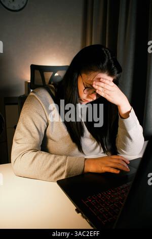 Müde Frau, die am Computer arbeitet, berührt ihren Kopf wegen Kopfschmerzen. Büroangestellte mit Migräne. Gestresster überlasteter Mitarbeiter mit Schmerzen o Stockfoto
