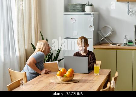 Mutter und Sohn teilen einen freudigen Moment, lachen und arbeiten an einem Laptop in der Küche. Stockfoto