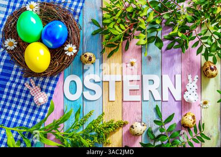 Bayern, Deutschland - 2. April 2025: Der Schriftzug OSTERN auf farbigem Holzuntergrund, umgeben von Osterdekorationen, frischem Grün und einem Osternest mit bunten Eiern *** der Schriftzug OSTERN auf farbigem Holzuntergrund, umgeben von Osterdekoration, frischem Grün und einem Osternest mit bunten Eiern Stockfoto
