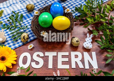 Bayern, Deutschland - 2. April 2025: Der Schriftzug OSTERN auf einem Holz Hintergrund, umgeben von Osterdekoration, frischem Grün und einem Osternest mit bunten Eiern *** der Schriftzug OSTERN auf einem Holz Hintergrund, umgeben von Osterdekoration, frischem Grün und einem Osternest mit bunten Eiern Stockfoto