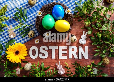 Bayern, Deutschland - 2. April 2025: Der Schriftzug OSTERN auf einem Holz Hintergrund, umgeben von Osterdekoration, frischem Grün und einem Osternest mit bunten Eiern *** der Schriftzug OSTERN auf einem Holz Hintergrund, umgeben von Osterdekoration, frischem Grün und einem Osternest mit bunten Eiern Stockfoto