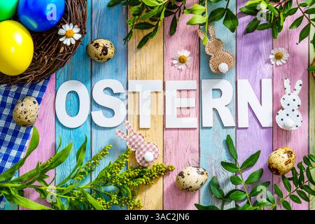 Bayern, Deutschland - 2. April 2025: Der Schriftzug OSTERN auf farbigem Holzuntergrund, umgeben von Osterdekorationen, frischem Grün und einem Osternest mit bunten Eiern *** der Schriftzug OSTERN auf farbigem Holzuntergrund, umgeben von Osterdekoration, frischem Grün und einem Osternest mit bunten Eiern Stockfoto