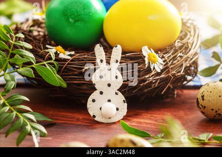 Bayern, Deutschland - 2. April 2025: Ein kleiner Osterhase vor einem bunten Osternest mit gefärbten Eiern, umgeben von Frühlingsblumen und Wachteleiern *** ein kleiner Osterhase vor einem bunten Osternest mit gefärbten Eiern, umgeben von Frühlingsblumen und Wachteleiern Stockfoto