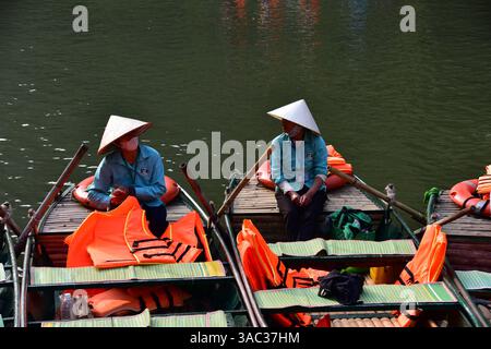 Vietnamesische Frauen mit Strohhüten in Holzbooten warten auf Touristen in Ninh Binh Stockfoto