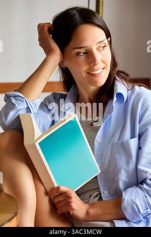 35-jährige Frau zu Hause, liest ein Buch, schaut zur Seite Stockfoto